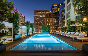 Rooftop pool at night, surrounded by lounge chairs and tall city buildings with lights in the background.