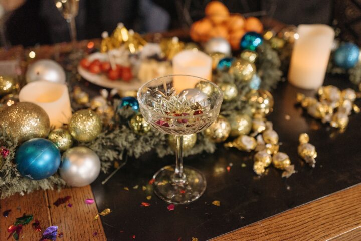 A festive table with candles, baubles, wrapped candies, a crystal glass, and holiday decorations scattered around.