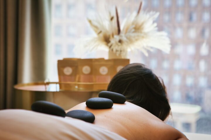 A person receives a hot stone massage in a spa, with three stones on their back and natural light coming through a window in the background.
