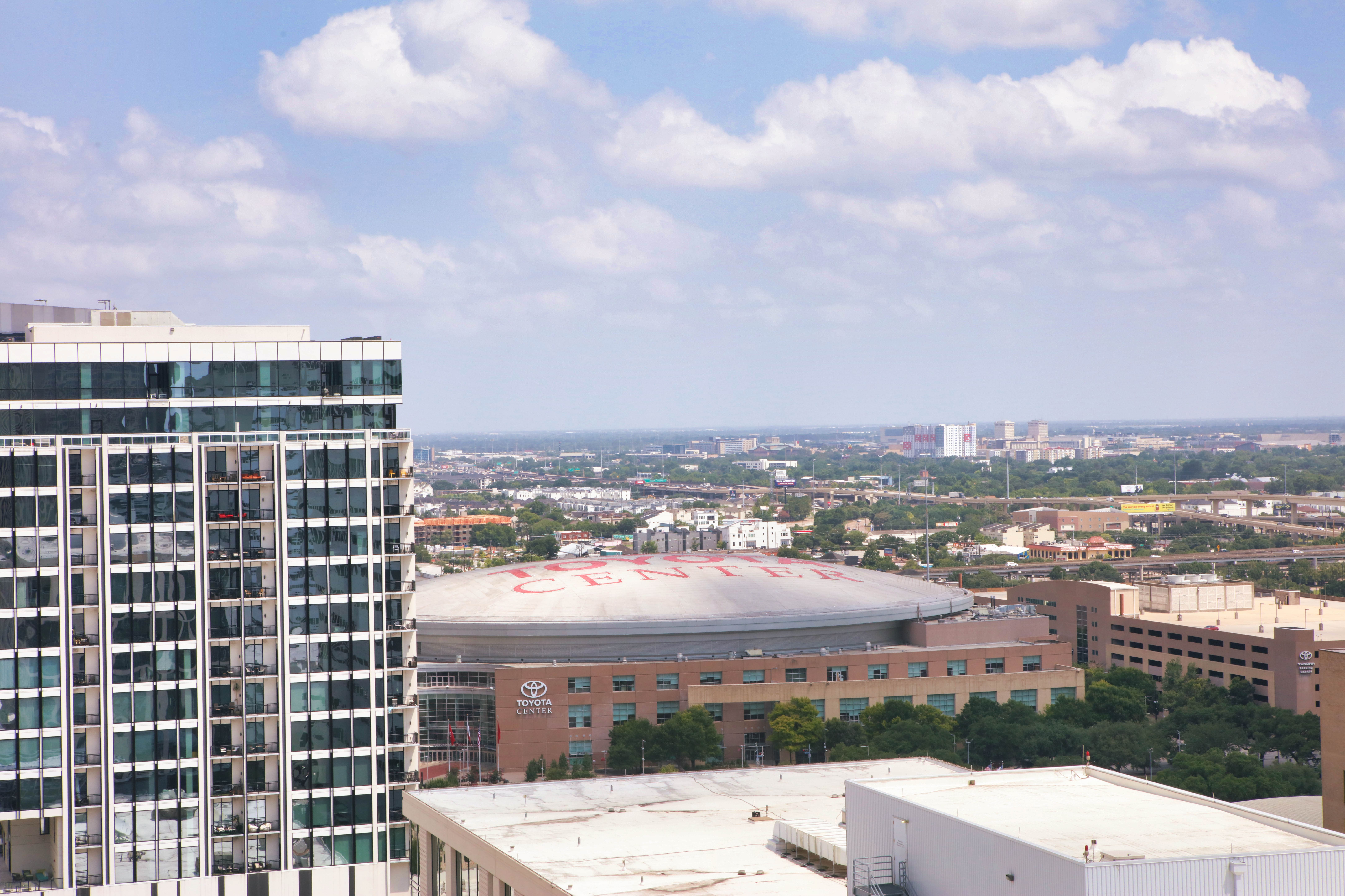 Aerial view of a city with a glass building and the Toyota Center arena under a blue sky with clouds.