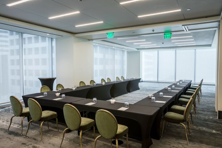 A modern conference room with U-shaped tables, green chairs, notepads, glasses, and large windows with city views.