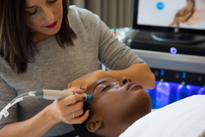 A woman receives a facial treatment with a handheld device while lying down in a clinic setting.