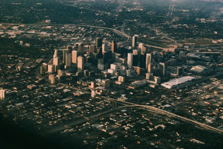 Aerial view of a downtown city skyline with tall buildings, highways, and surrounding neighborhoods under daylight.
