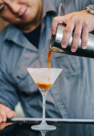 Bartender pouring a cocktail from a shaker into a martini glass at a bar.