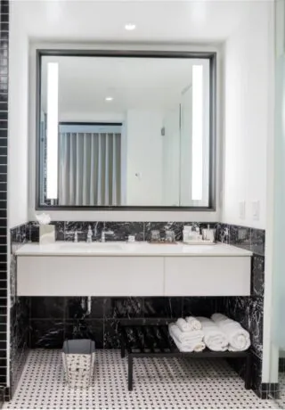 Modern bathroom with a glass shower, large mirror, black and white tiles, double sink, towels on a bench, and frosted glass door.